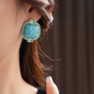 Close-up of vintage gold earrings with turquoise stone and blue rhinestones on model