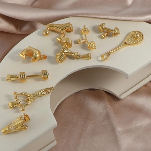 Golden stainless steel sports pendants featuring dumbbell and racket shapes on silk fabric