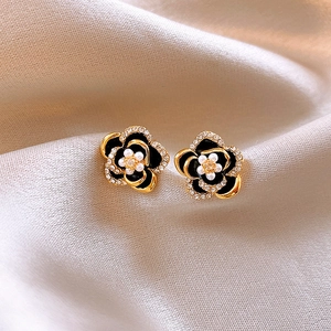 Detailed close-up of camellia-shaped enamel earrings resting on soft beige silk fabric