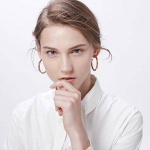 Front close-up of a model wearing large polished gold stainless steel C-shaped hoop earrings