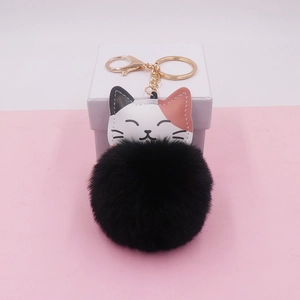Detail view of a cute cartoon cat keychain with black pompom and gold hardware