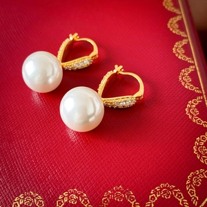 Gros plan de boucles d'oreilles dorées avec perles et cristaux sur une boîte cadeau rouge