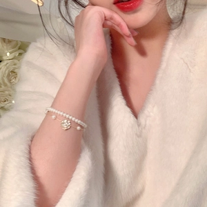 Elegante pulsera de doble capa con perlas y camelia en la muñeca de una modelo