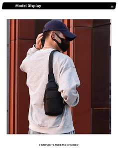 Men's minimalist black nylon chest bag worn by a model against a textured wall backdrop
