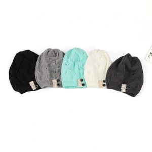 Detailed view of knitted beanies with hollow leaf patterns and decorative lace buttons.