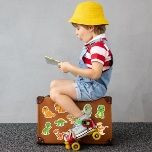 Cute cartoon dinosaur stickers applied on a vintage suitcase in a playful lifestyle scene
