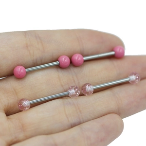 Close-up of pink heart-shaped tongue rings with glitter finish held in a hand for scale