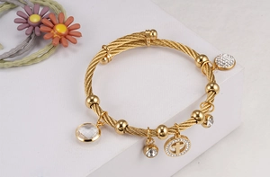 Detail of twisted 18K gold plated bangle with sparkling crystal cross charms and metal beads