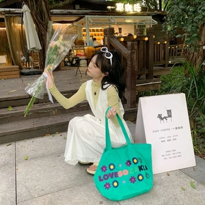Close-up of green canvas tote bag featuring vibrant floral embroidery and bold lettering