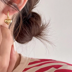 Close-up of a gold heart pendant hoop earring worn by a model in soft lighting
