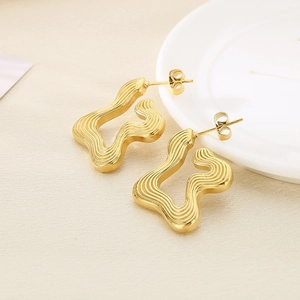 Detail view of golden irregular wave texture stud earrings on a ceramic tray