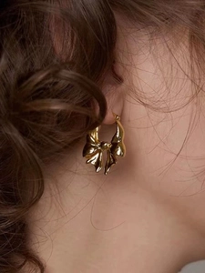 Close-up of golden bow-shaped brass earring worn by a model with a polished finish