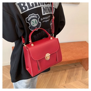 Detail of red leather crossbody bag with vintage gold buckle on a warm background