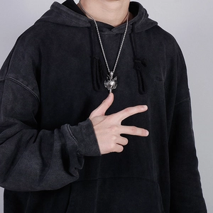Detailed view of a silver wolf head pendant necklace on a model wearing a black hoodie