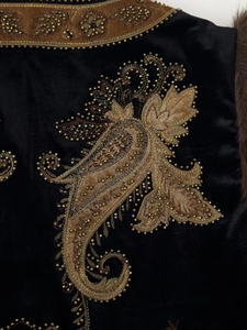 Macro shot of gold paisley embroidery and intricate beadwork on premium black velvet fabric