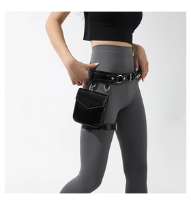 Close-up of black PU leather leg bag with metal buckles and rivets on grey leggings