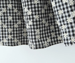 Detail of black and white vichy check fabric with white flower embroidery and hemmed edge