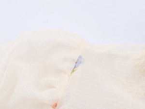 Detailed close-up of beige woven fabric with floral embroidery on the sleeve seam