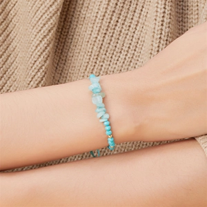 Detail eines handgefertigten Armbands mit Türkissteinen, blauem Kordelzug und Goldperle