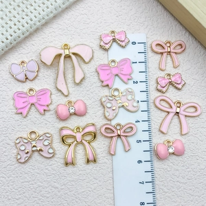 Various pink and gold bow pendants with rhinestones shown on a scale for size reference