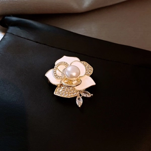 Macro detail of 14k gold-plated pearl flower brooch with enamel petals and rhinestones