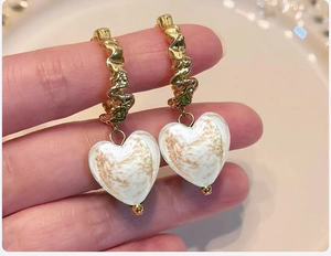 Macro detail of gold twisted hoop earrings featuring white heart pendants with gold foil