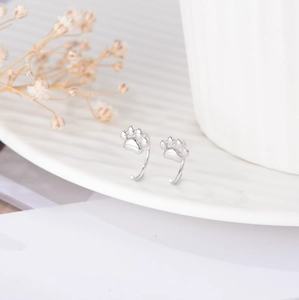 Macro shot of silver cat paw earrings on a white plate with delicate dried flowers