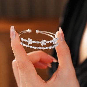 Détail d'un bracelet jonc double en argent avec fleurs en zircon tenu en main