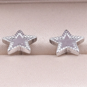 Macro shot of silver star stud earrings with radial patterns on beige silk jewelry box