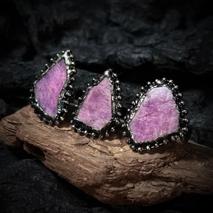 Dettaglio macro di tre anelli vintage con rubini rosa grezzi e metallo nero retrò