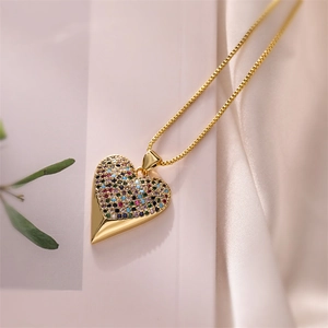 Macro shot of gold heart pendant featuring colorful zircons on white silk background