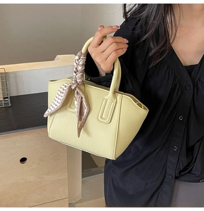 Detail of yellow lychee texture bucket bag with silk scarf on handle held by model