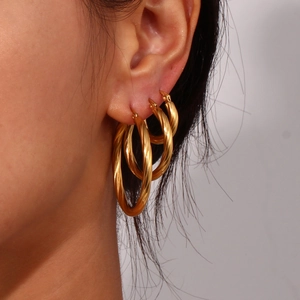 Detail view of triple stacked golden twisted C-shaped hoop earrings on model ear