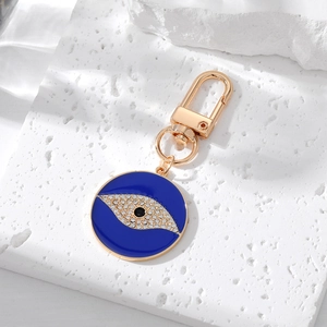 Blue evil eye keychain with sparkling rhinestones and golden metal hardware on stone