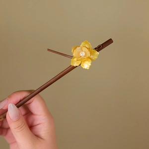 Detailed view of wood hair pin featuring yellow resin flower and white pearl accents