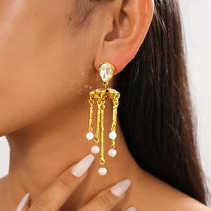 Detail view of gold tassel earrings with rhinestones and white pearls on a female model