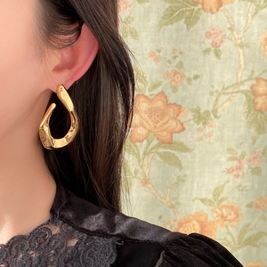 Polished gold twisted U-shaped earring shown on model with vintage floral background