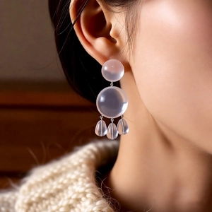 Detail of transparent frosted resin drop earrings worn by a model in warm lighting