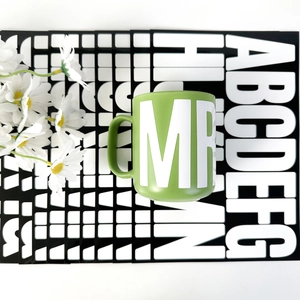 Top-down view of a green ceramic mug featuring white MR lettering on a graphic background