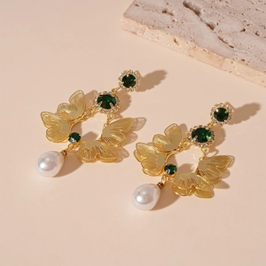 Detailed shot of golden butterfly earrings with green stones and white teardrop pearls