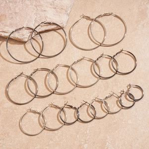 Polished silver metal hoop earring set in various sizes on a natural stone background