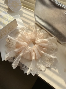 Detailed view of champagne satin scrunchie with white floral embroidery lace edge