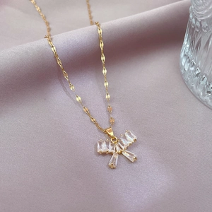 Macro detail of gold butterfly necklace with rectangular zircons on pink satin background