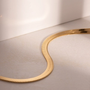Detailed macro view of an S-shaped flat gold snake chain necklace on white texture