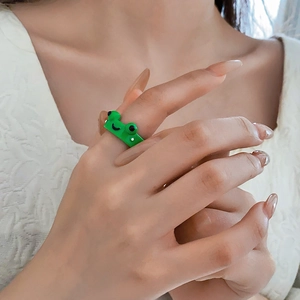 Close-up of a cute green resin frog ring with black eyes and smile on a finger