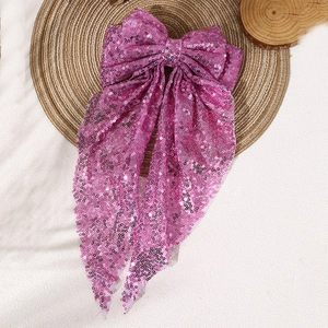 Close-up of pink sequin oversized bow hair clip with streamers on woven mat