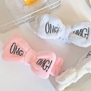 Close-up of three plush bow headbands in blue, pink, and white with OMG embroidery