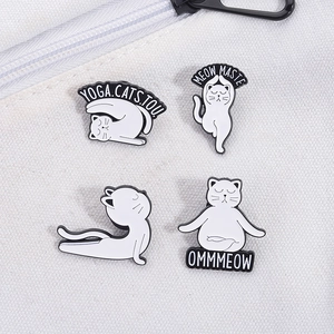Set of four black and white yoga cat enamel pins displayed on a canvas backpack strap