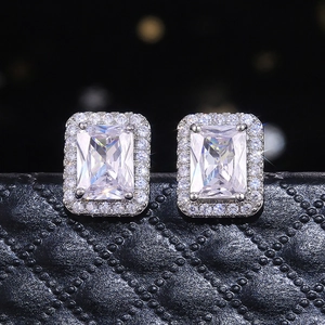 Detailed close-up of emerald-cut zircon stud earrings with halo setting on a black box