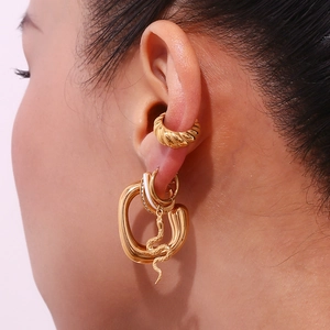 Close-up of gold snake pendant earrings and heart charms layered on a model's ear